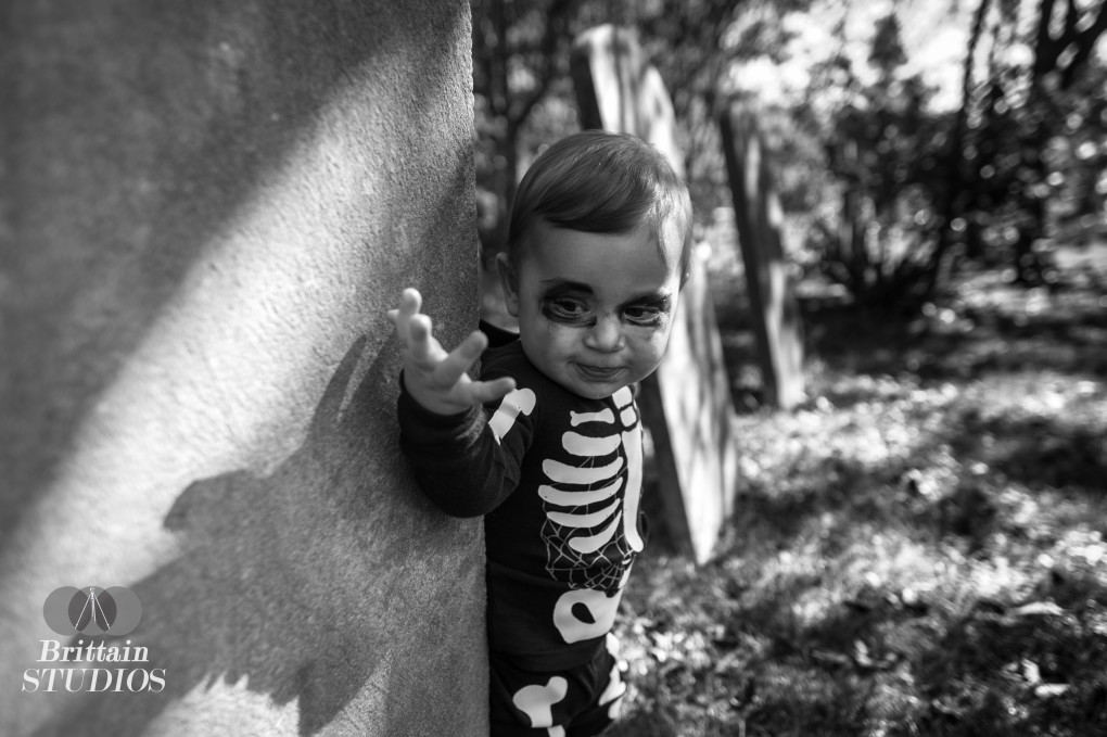 October 18th – Charlie’s grandparents were nice enough to recognize the enormity of this venture long before October started, so they supplied us with several of the costumes. They gave Charlie the Tiger costume which was featured a few weeks ago as well as the Skeleton costume in today’s picture. We frequently drive past a small graveyard in Toms River with headstones no younger than 110 years old. It has been seemingly abandoned for quite some time, as half of the headstones are knocked over, the ground is covered in small cacti, and a pest control company currently owns the chapel adjacent to it. We tried a few different locations with Caroline hiding and holding Charlie just out of frame, but we loved the pose he struck in this one as well as the light coming through the trees.